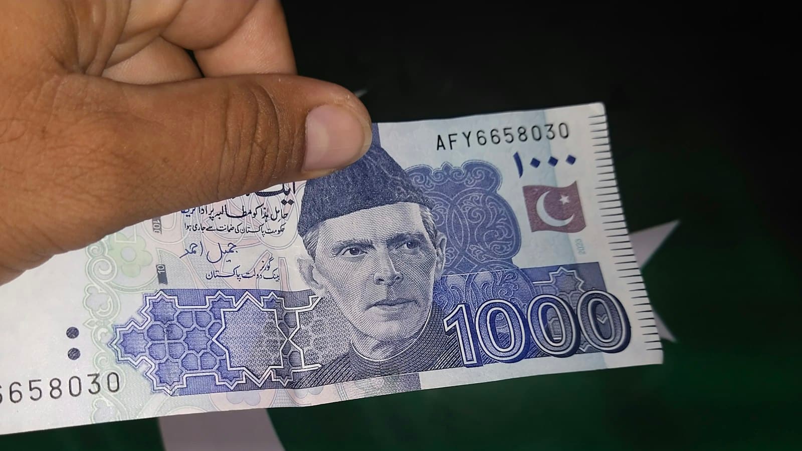 A hand holding a Pakistani 1,000-rupee banknote