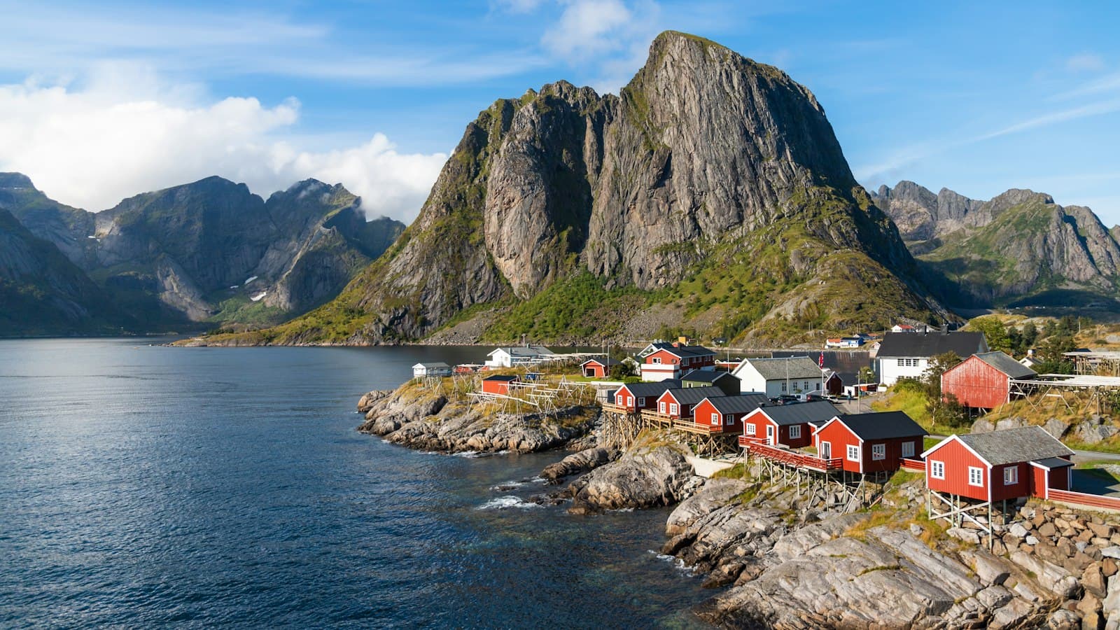 Red fishing cabins on a rocky shore beneath a mountain in Lofoten, Norway