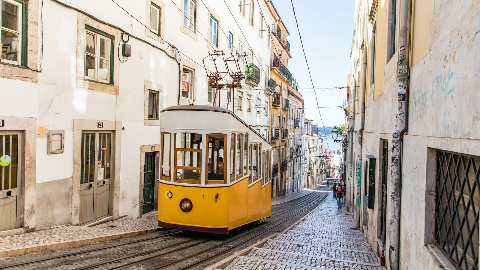 A yellow tram climbing a narrow cobbled street in Lisbon