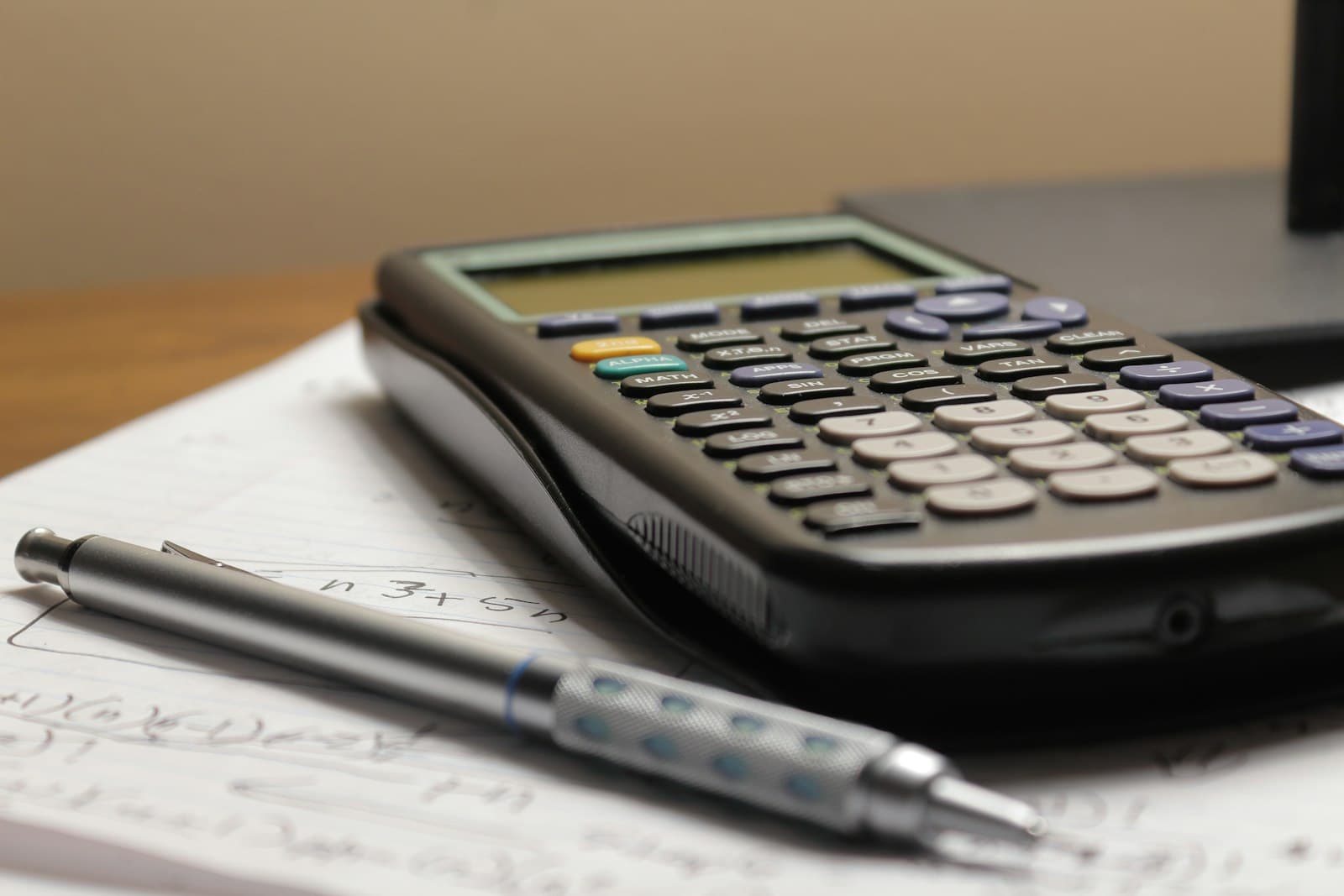 A calculator and pen resting on handwritten notes while working out the funds needed for a visa application